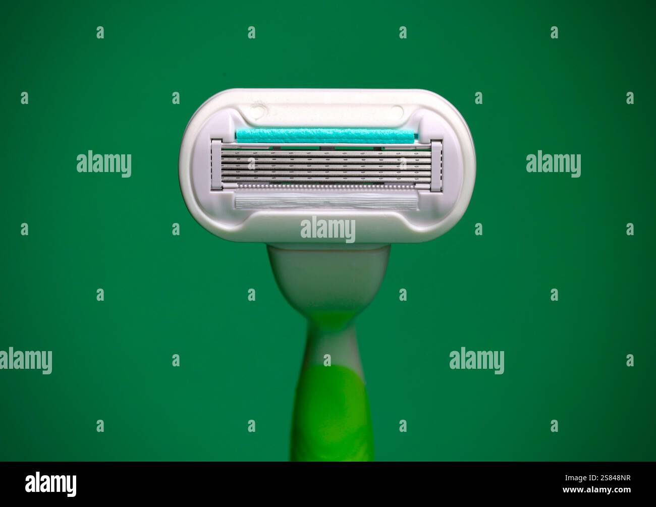 Gros plan d'une tête de rasoir avec un manche vert sur un fond vert éclatant, mettant en valeur son design épuré et net. Banque D'Images