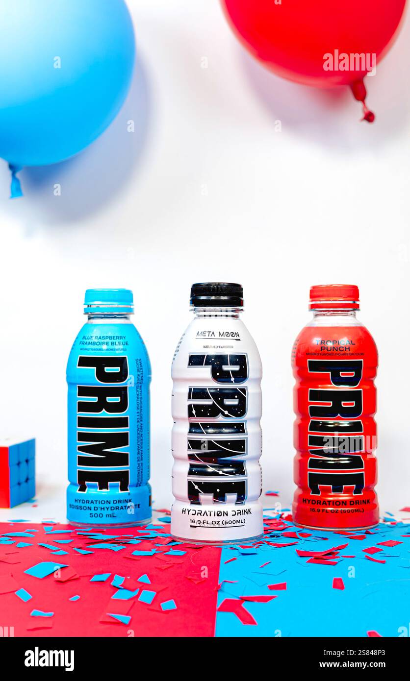 Trois bouteilles de boisson hydratante Prime colorées présentées avec des ballons rouges et bleus festifs et des confettis. Banque D'Images
