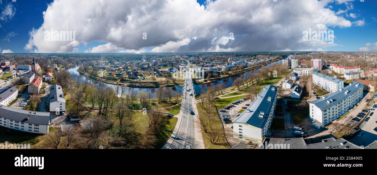 Vue aérienne panoramique d'une petite ville divisée par une rivière sinueuse, avec un pont, des espaces verts et une église avec une grande flèche sous un clou spectaculaire Banque D'Images