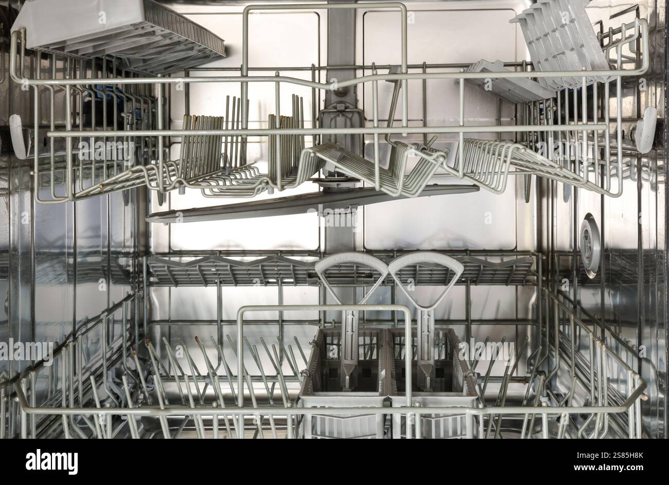 Intérieur d'un lave-vaisselle vide et propre en acier inoxydable avec deux supports à ustensiles et panier en plastique. Vue de face. Banque D'Images