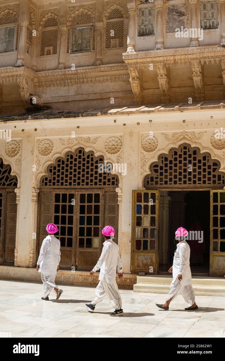 JODHPUR, INDE - 18 MARS 2024 : trois hommes indiens en turbans roses et robes traditionnelles marchant dans l'arrière-cour du fort de la ville Banque D'Images