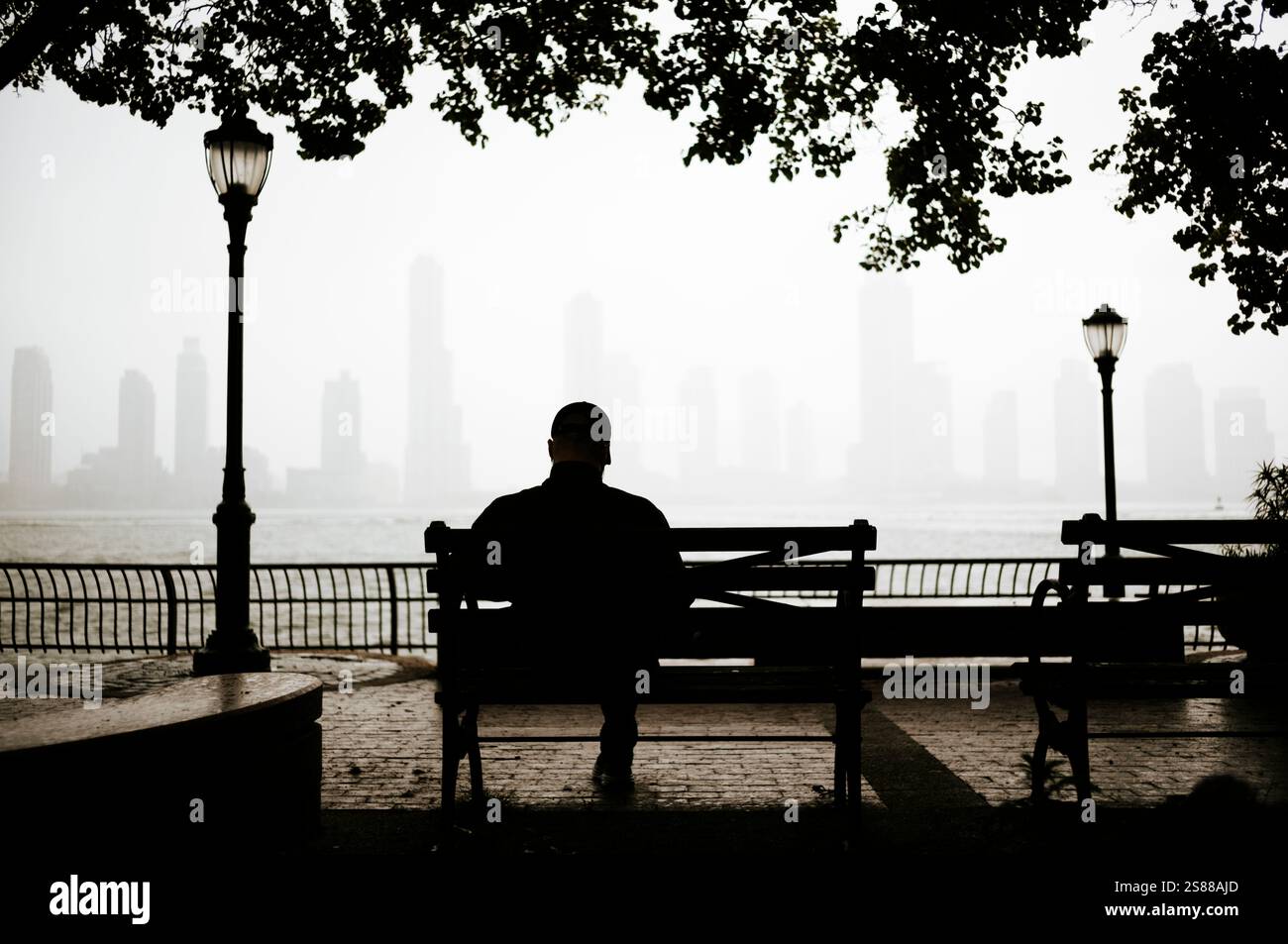 Silhuete d'un homme assis sur un banc avec vue de Manhattan ville en arrière-plan, New York, États-Unis Banque D'Images