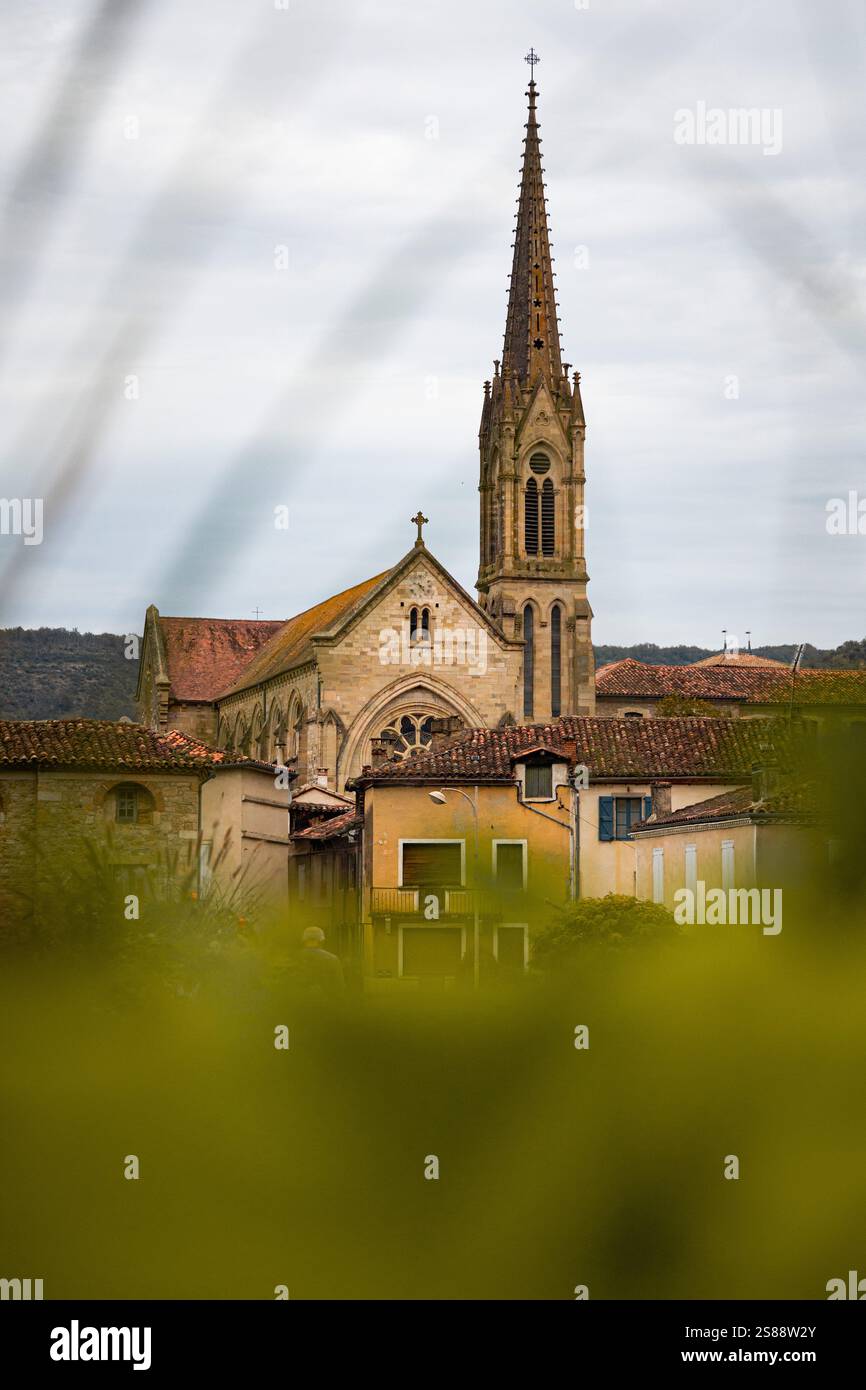 Image captivante de la flèche de l'église de style gothique à Saint-Antonin-Noble-Val, Occitanie, France, encadrée par une douce verdure au premier plan Banque D'Images