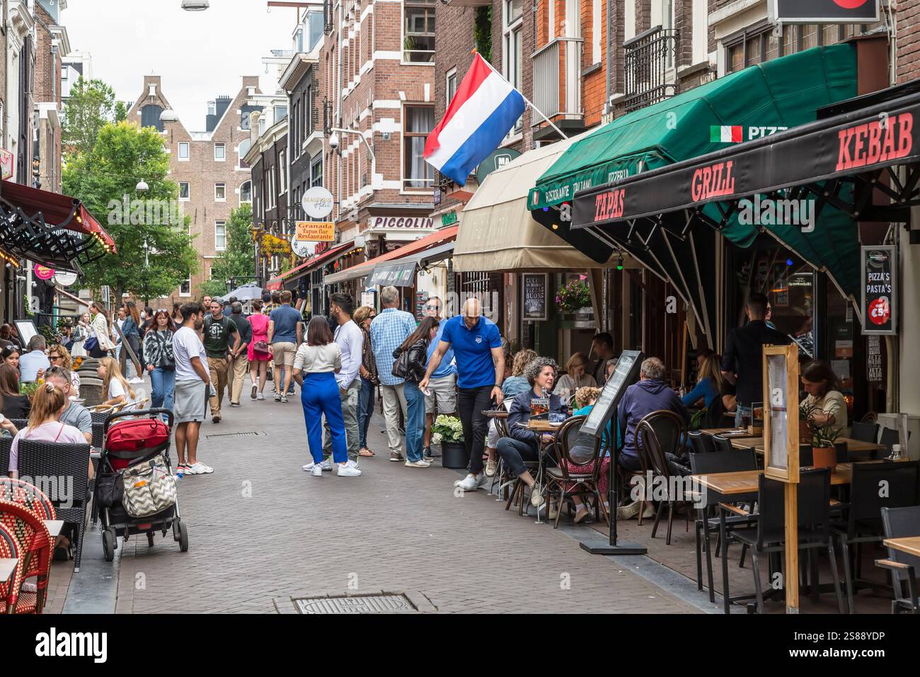 Les gens marchent et font du vélo devant des terrasses confortables dans une rue étroite d'Amsterdam. Banque D'Images