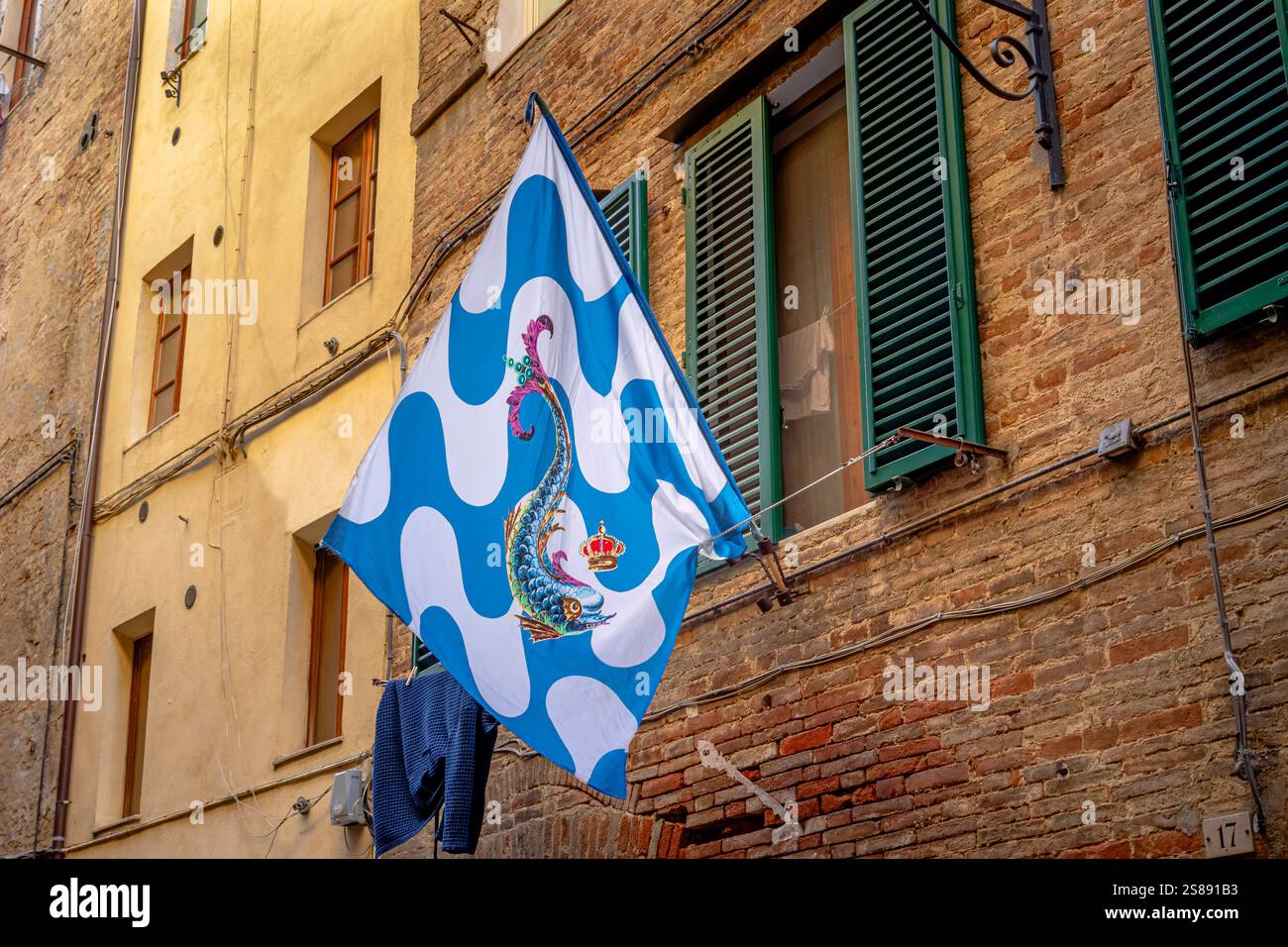 Le drapeau de la Contrada Onda , Wave Contrada , suspendu au mur d'un mur de bâtiment le long de la via Sant'Agata à Sienne , Italie Banque D'Images