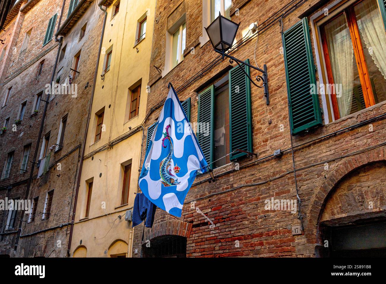Le drapeau de la Contrada Onda , Wave Contrada , suspendu au mur d'un mur de bâtiment le long de la via Sant'Agata à Sienne , Italie Banque D'Images