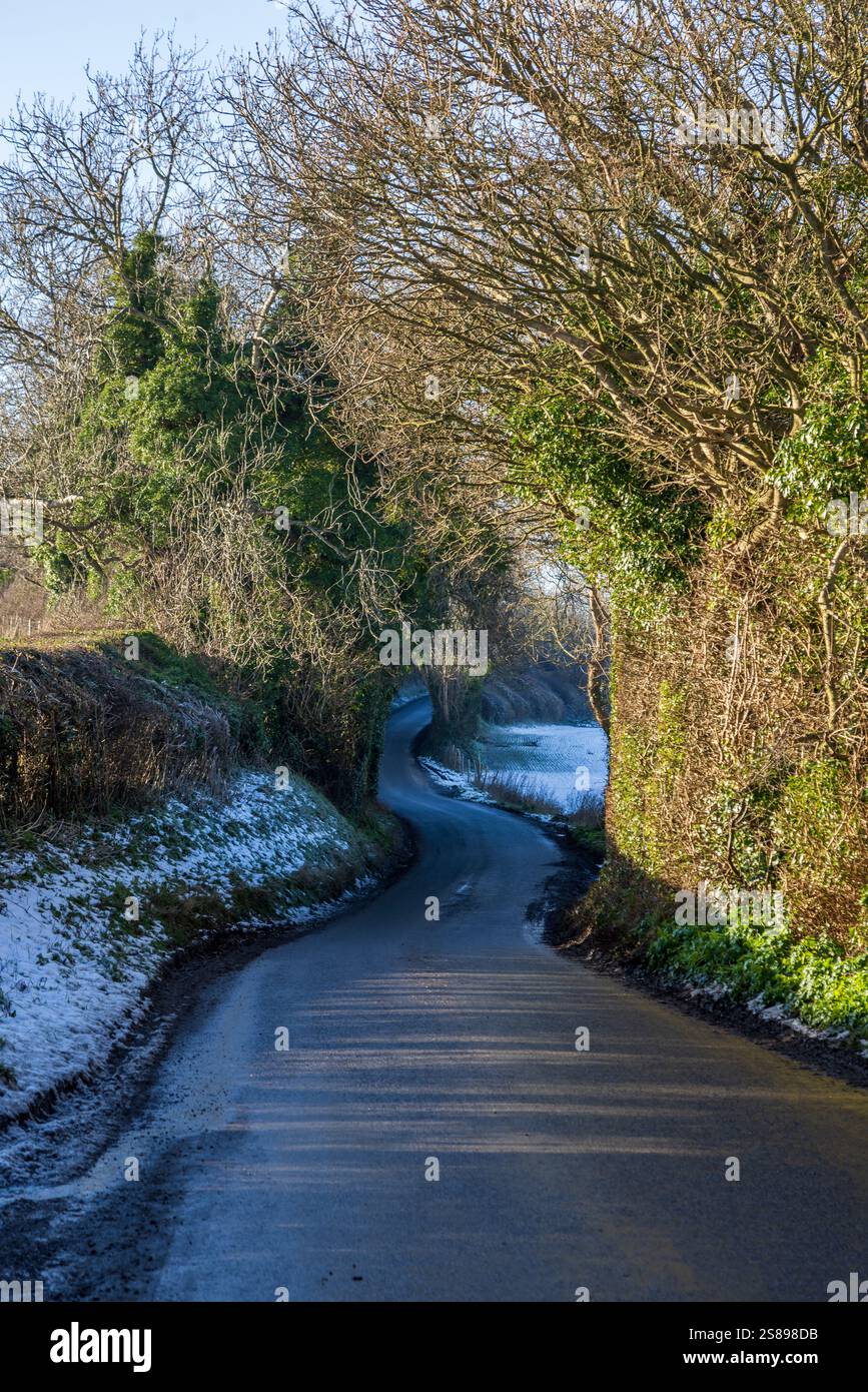 Une route de campagne dans le Sussex rural, sur un jour d'hiver suny avec de la neige sur les bords Banque D'Images