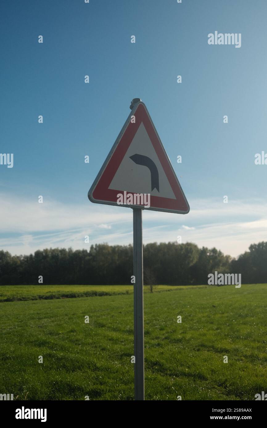 Un panneau triangulaire avec une flèche rouge pointant vers la droite. Le signe est dans un champ herbeux avec un ciel bleu clair Banque D'Images