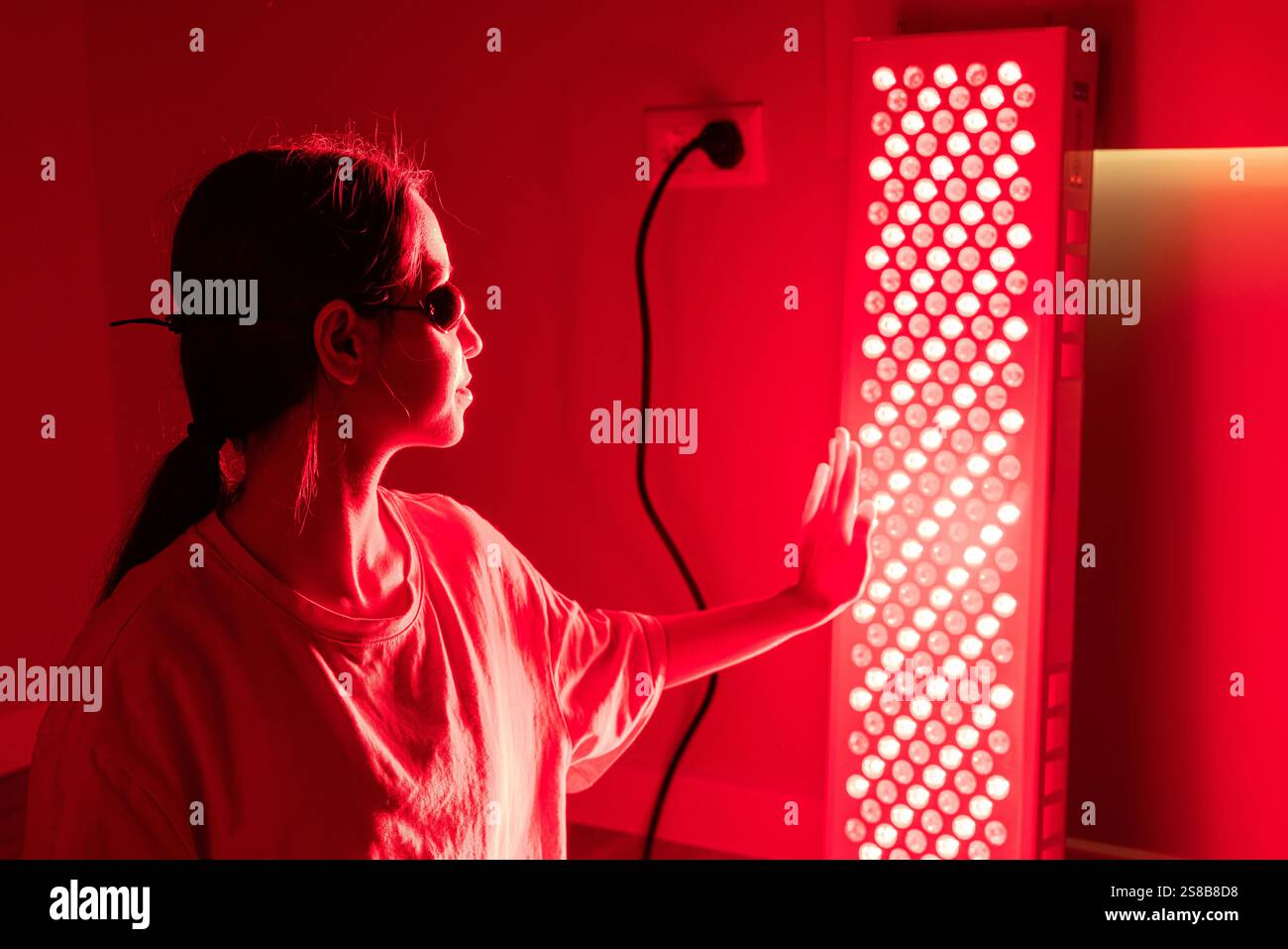 Vue rapprochée d'une jeune femme utilisant un équipement de luminothérapie rouge à l'intérieur Banque D'Images
