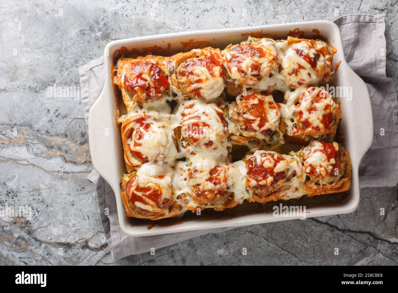 Sliders faits maison farcis de boulettes de viande, recouverts de sauce tomate et de fromage râpé gros plan dans un plat de cuisson sur une table. vue horizontale de dessus fr Banque D'Images