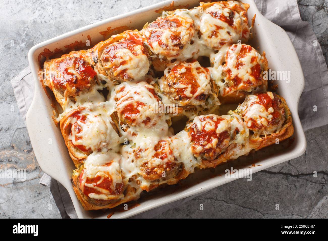 Sandwichs chauds faits de petits pains fourrés de boulettes de viande, garnis de sauce tomate et saupoudrés de gros plan de fromage dans un plat allant au four sur une table. Banque D'Images