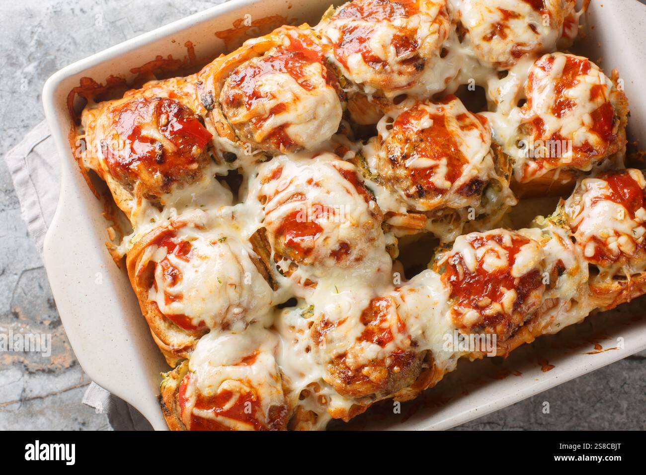 Petits pains cuits farcis de boulettes de viande, recouverts de sauce tomate et saupoudrés de gros plan de fromage dans un plat allant au four sur la table. haut horizontal v Banque D'Images