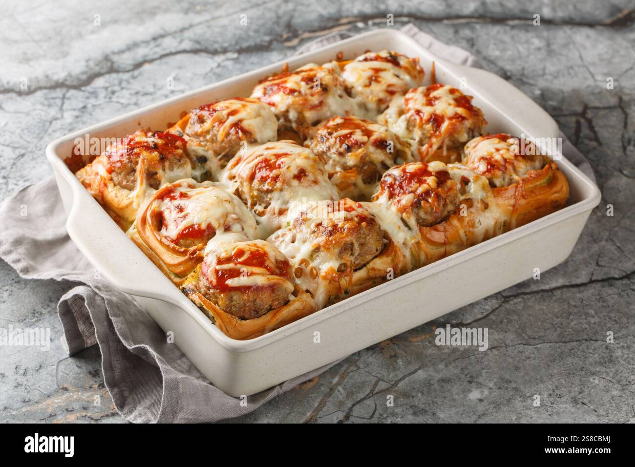 Sandwichs chauds faits de petits pains fourrés de boulettes de viande, garnis de sauce tomate et saupoudrés de gros plan de fromage dans un plat allant au four sur une table. Banque D'Images