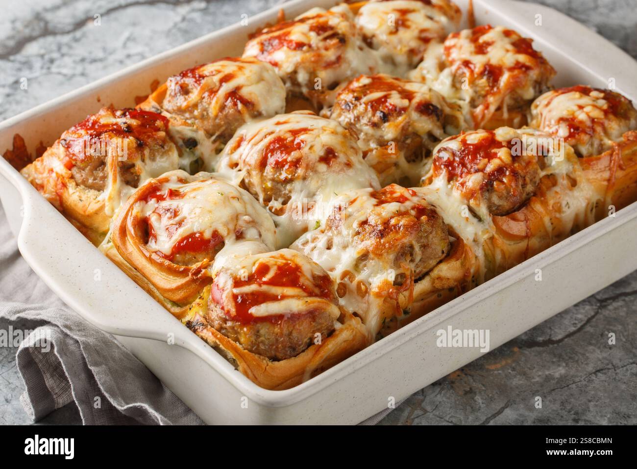 Petits pains cuits farcis de boulettes de viande, recouverts de sauce tomate et saupoudrés de gros plan de fromage dans un plat allant au four sur la table. horizontal Banque D'Images
