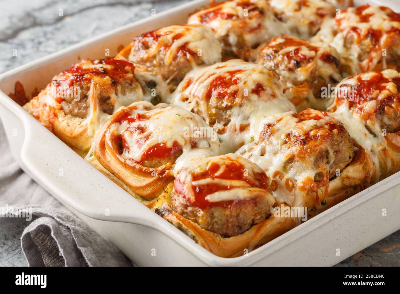 Sliders faits maison farcis de boulettes de viande, recouverts de sauce tomate et de fromage râpé gros plan dans un plat de cuisson sur une table. horizontal Banque D'Images