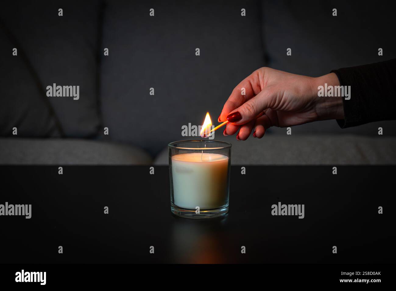 Femme allumant une bougie parfumée avec une allumette sur un fond sombre, créant une atmosphère chaleureuse et confortable Banque D'Images