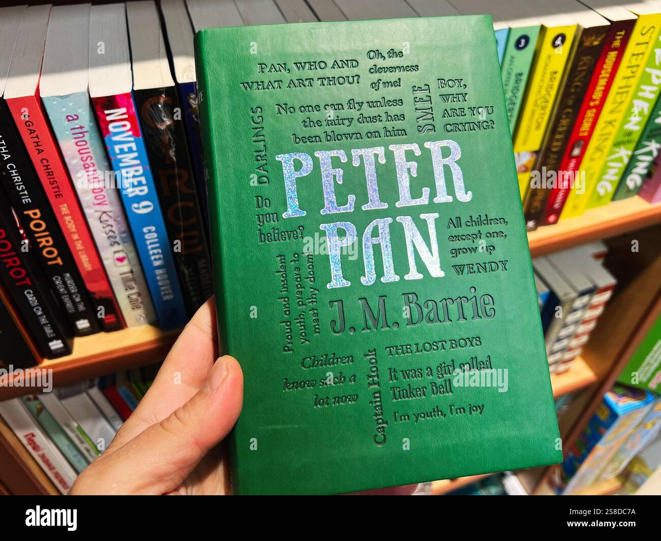 Kiev, Ukraine - 21 janvier 2025 : un gros plan d'une main tenant le livre J M Barrie 'Peter Pan' sur fond d'étagères remplies de divers Banque D'Images