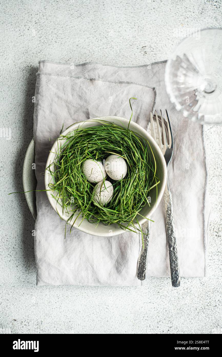 Vue de dessus d'une table de Pâques simple mais élégante avec un bol avec un nid d'herbe verte fraîche et trois œufs mouchetés. Une paire de vintage pour Banque D'Images