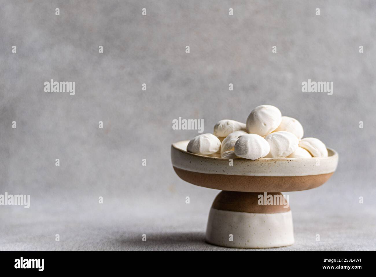 Un charmant arrangement de mini guimauves zephyr maison exposées sur un socle en céramique bicolore, créant un minimaliste élégant et accueillant Banque D'Images