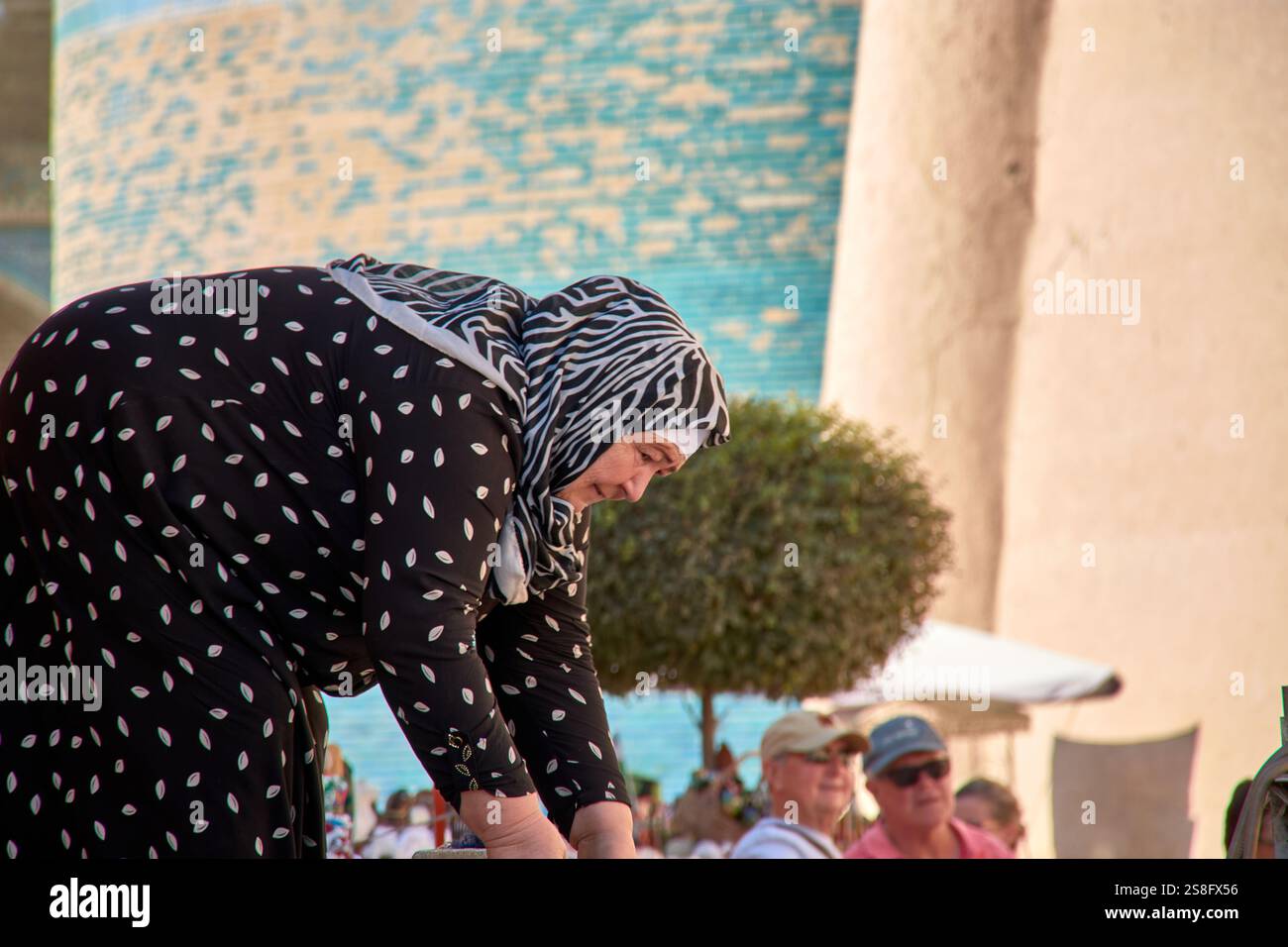 Kihva, Ouzbékistan ; septembre,21,2024:une femme musulmane âgée à Khiva, Ouzbékistan, alors qu'elle se lève après avoir ramassé des tissus de soie qu'elle vend aux touristes. Banque D'Images