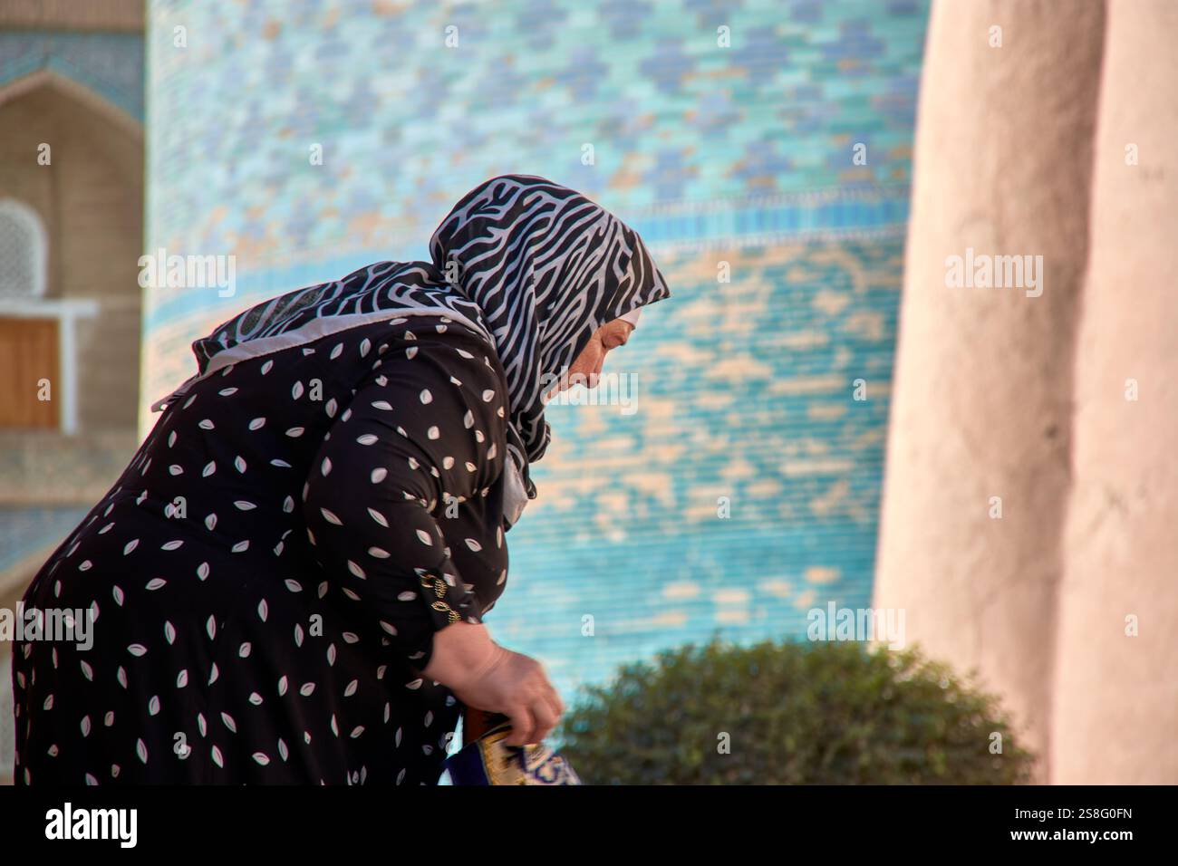 Kihva, Ouzbékistan ; septembre,21,2024:une femme musulmane âgée à Khiva, Ouzbékistan, alors qu'elle se lève après avoir ramassé des tissus de soie qu'elle vend aux touristes. Banque D'Images