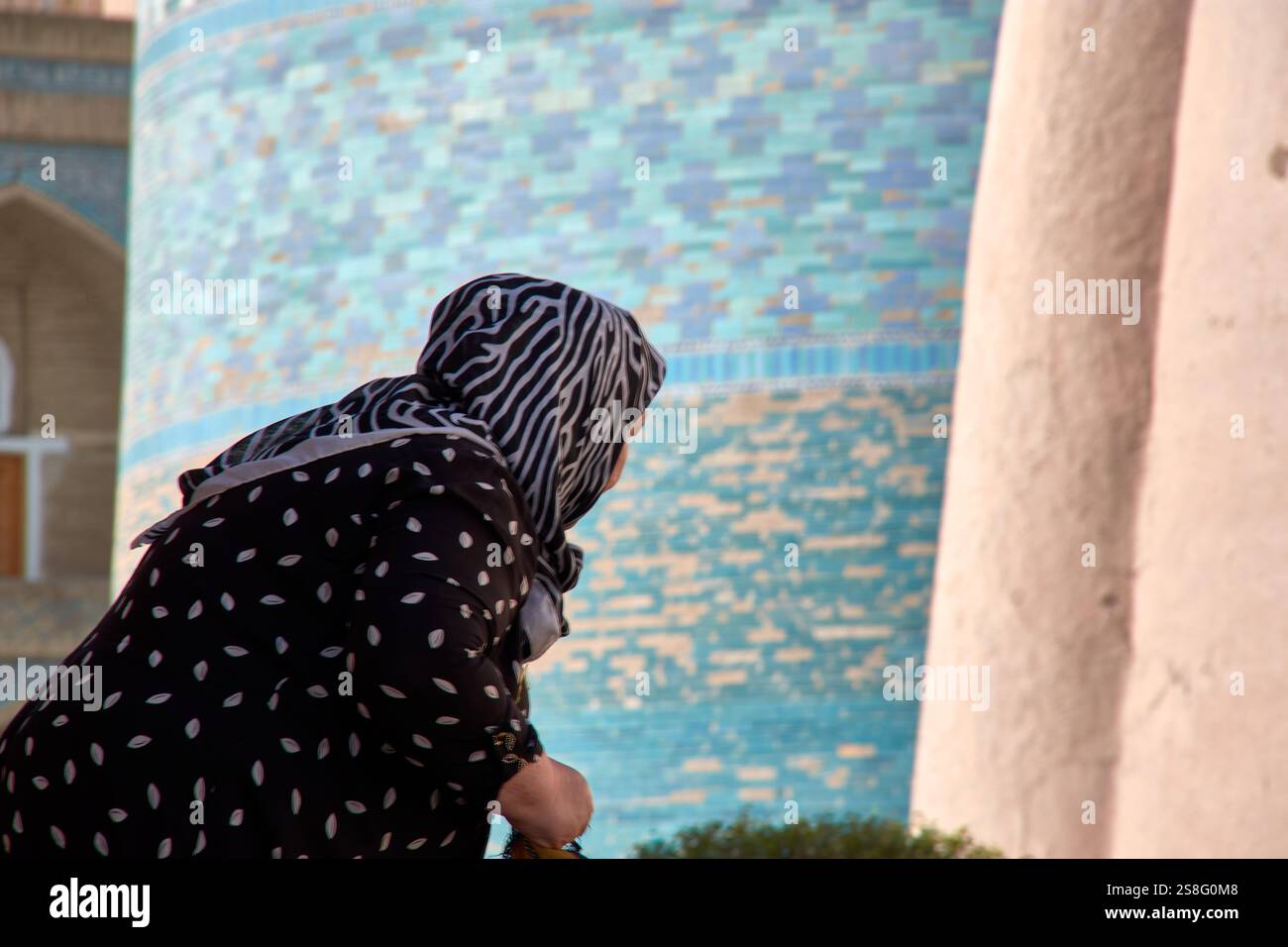 Kihva, Ouzbékistan ; septembre,21,2024:une femme musulmane âgée à Khiva, Ouzbékistan, alors qu'elle se lève après avoir ramassé des tissus de soie qu'elle vend aux touristes. Banque D'Images