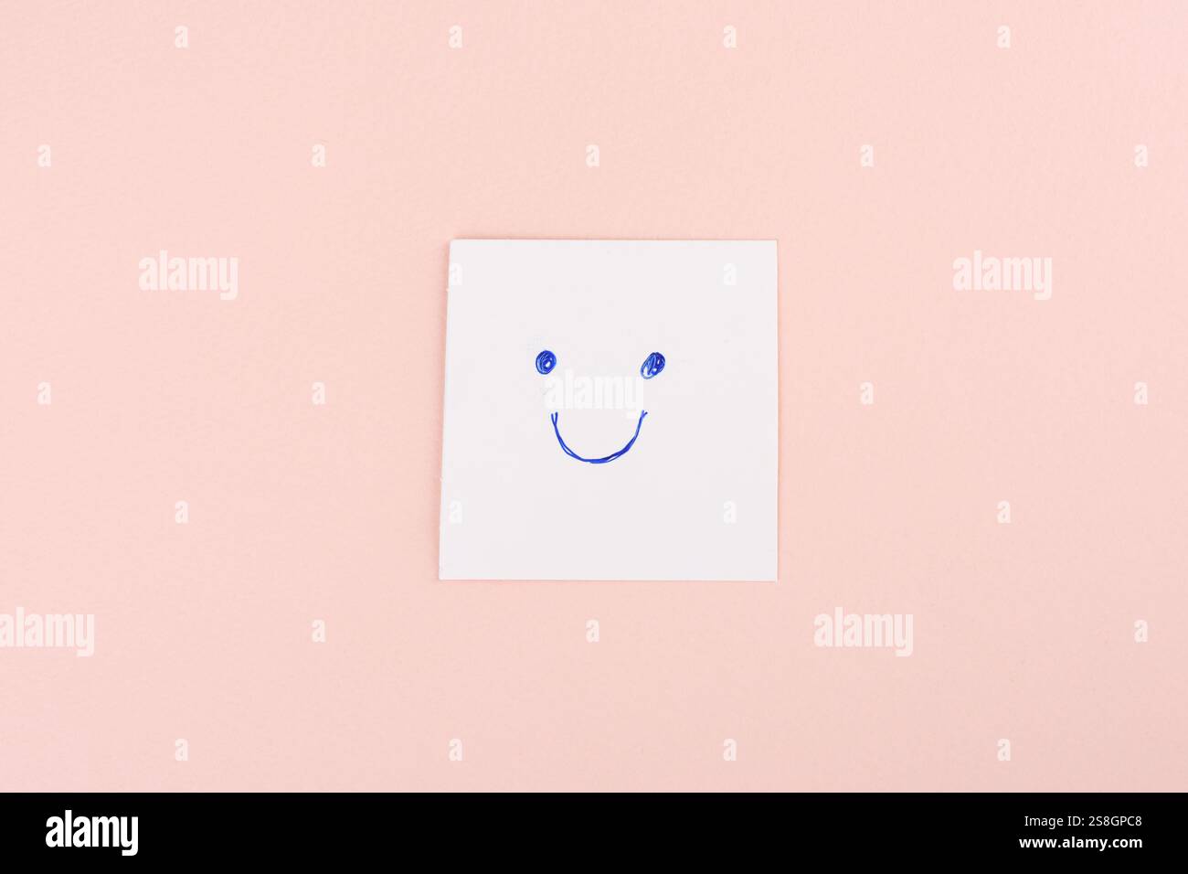 Papier blanc avec un visage smiley bleu dessiné à la main, placé sur un fond rose pastel. Concept de positivité et de simplicité Banque D'Images