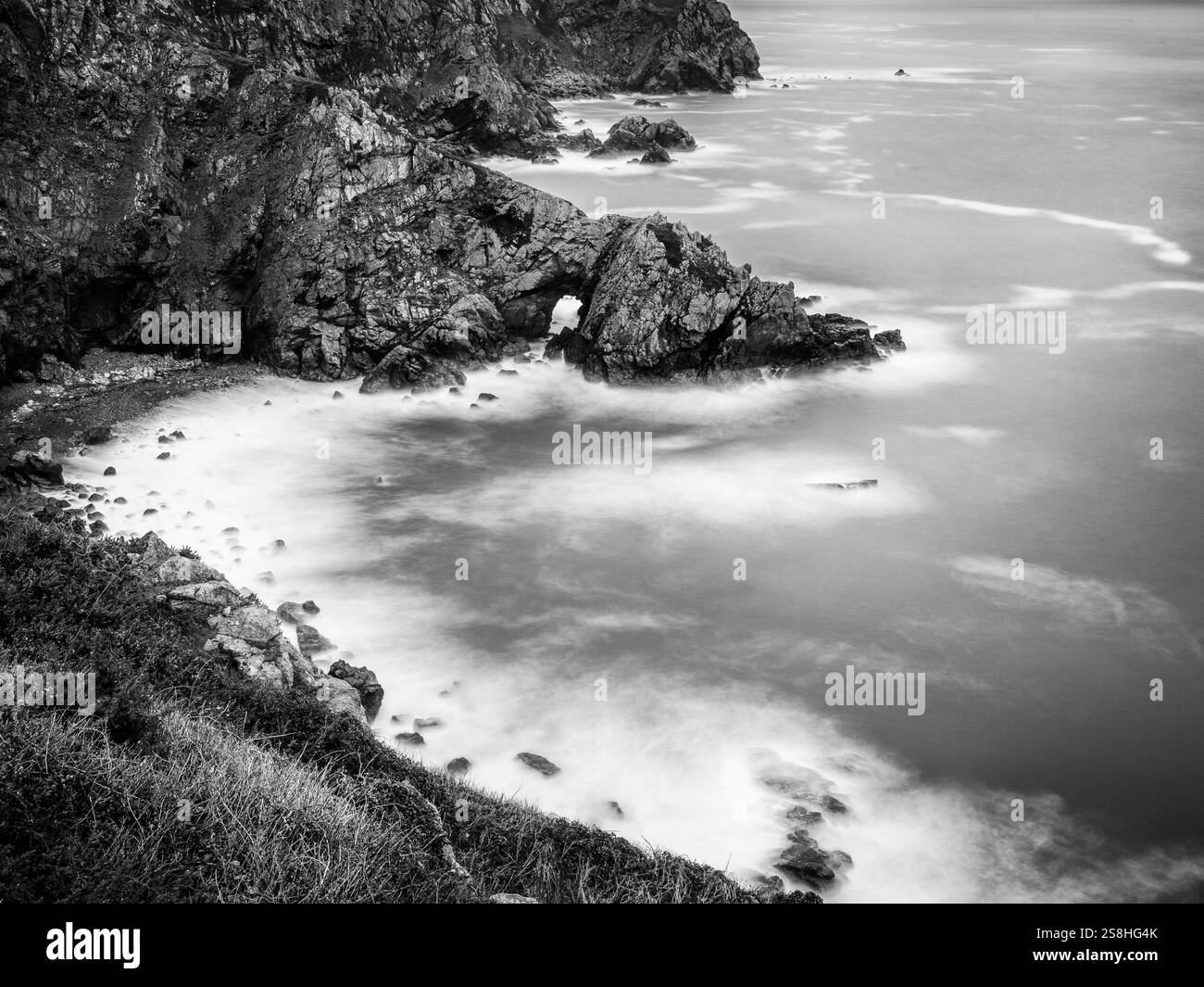 Falaises de granit accidentées, avec arche et mer floue longue exposition, sur la côte sud de Guernesey, îles Anglo-Normandes. Banque D'Images