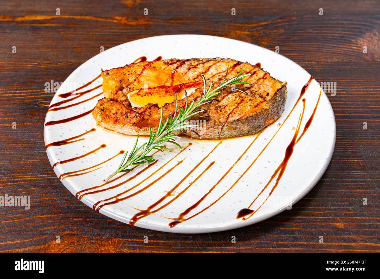Un filet de saumon magnifiquement cuit garni de romarin se trouve sur une assiette blanche. Le plat présente une présentation délicieuse avec glaçage balsamique, pe Banque D'Images