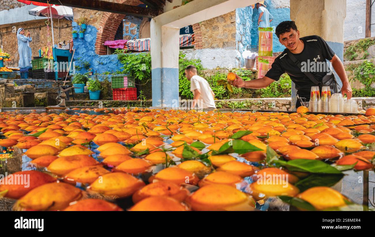 Chefchaouen, Maroc. Vieux lavoir maison pleine eau de source utilisée pour garder les oranges froides avant la préparation du jus. Un marocain montrant une orange fraîche. Banque D'Images
