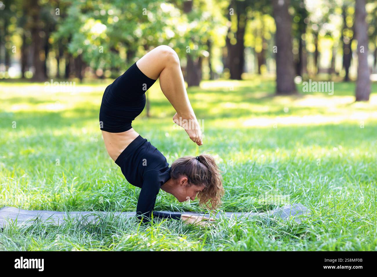 Jeune femme faisant de l'exercice vrischikasana, support d'avant-bras, pratiquant le yoga en vêtements de sport sur tapis dans le parc Banque D'Images