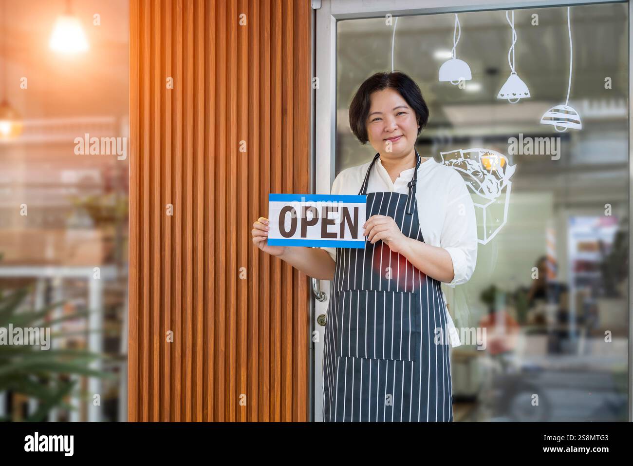 Concept réussi d'entrepreneur PME propriétaire de petite entreprise. Femme asiatique confiante tenant un signe ouvert, portant un tablier, debout devant le café Banque D'Images