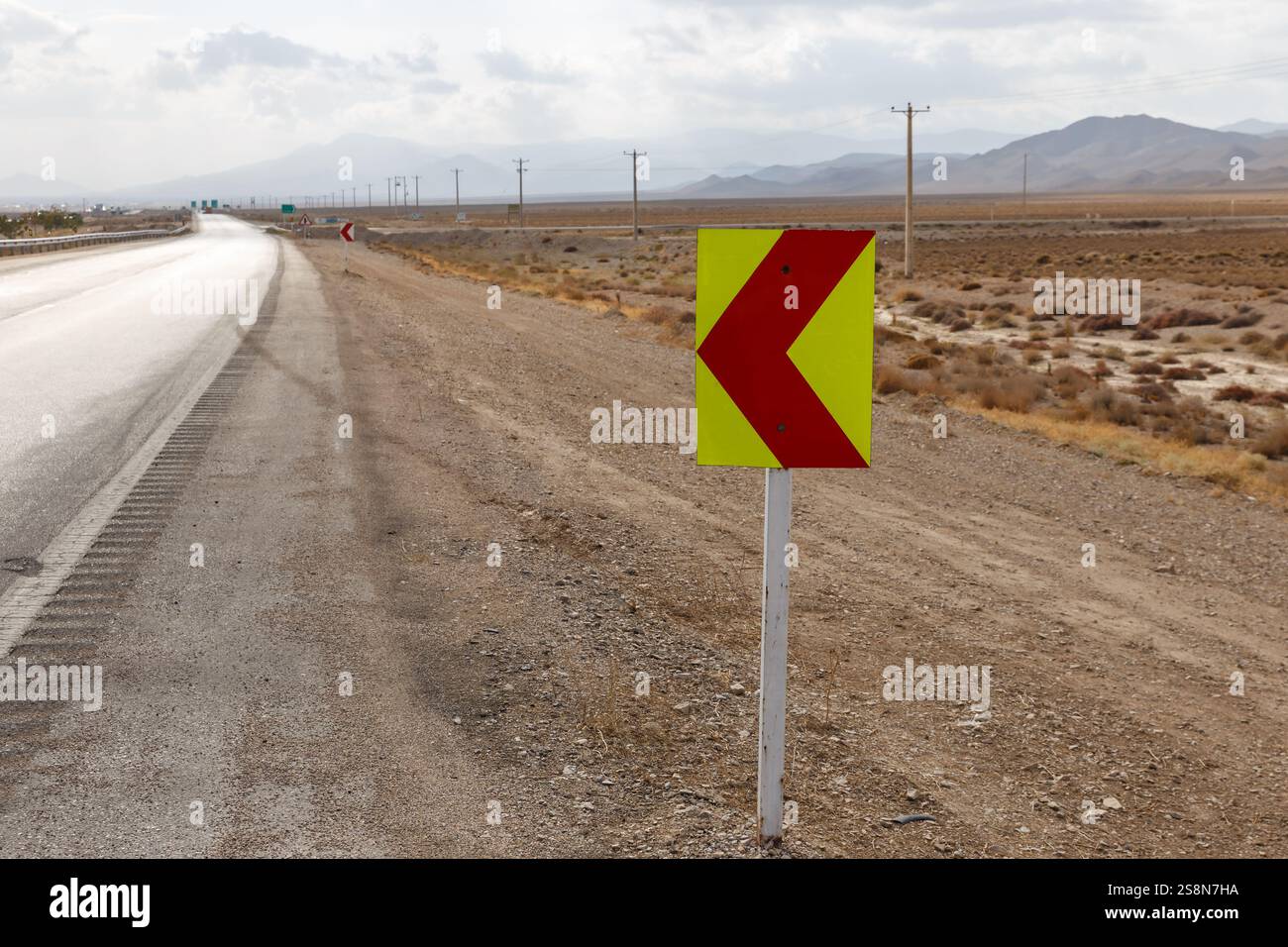 Un panneau rouge et jaune vif indiquant un virage à gauche est vu à côté de la route Gorgan Bojnord en Iran, avec des montagnes visibles au loin. Banque D'Images