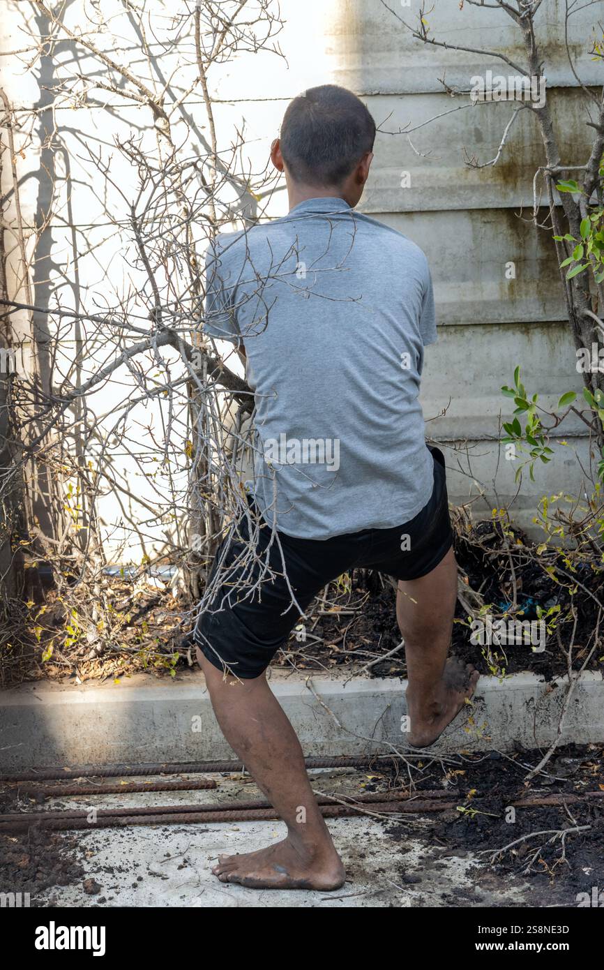 SAMUT PRAKAN, THAÏLANDE, OCT 03 2024, Un homme pieds nus tente de tirer un arbre du sol Banque D'Images