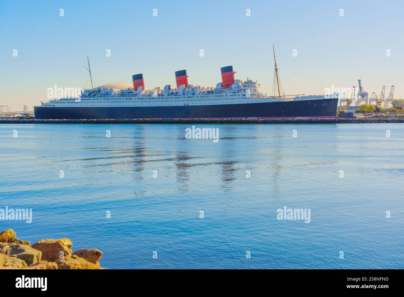 Long Beach, Californie - 15 janvier 2025 : vue sur le navire historique Queen Mary amarré à long Beach, reflétant les eaux calmes sous un ciel clair. Banque D'Images