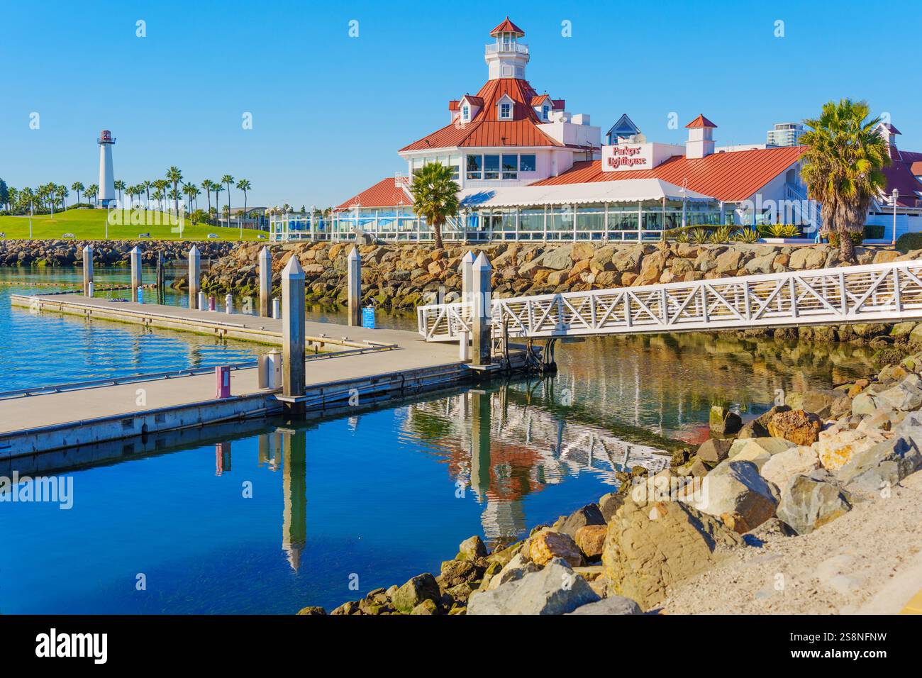 Long Beach, Californie - 15 janvier 2025 : vue panoramique sur un port avec un phare et un restaurant reflétés dans l'eau, avec un ciel clair et Banque D'Images