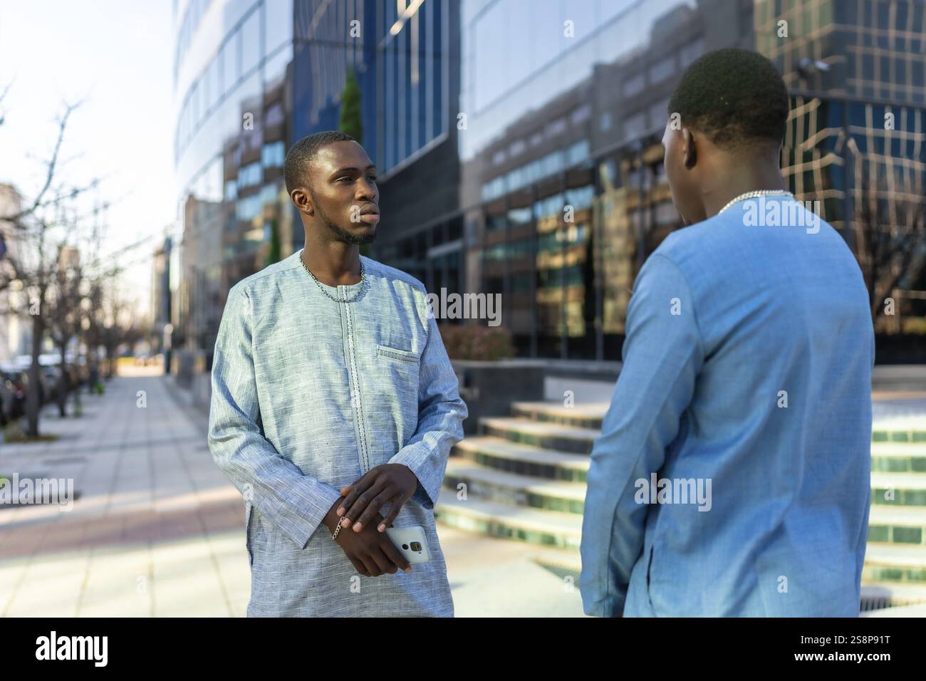 Deux hommes d'affaires sénégalais en tenue dashiki traditionnelle ont une conversation à l'extérieur d'un immeuble de bureaux moderne Banque D'Images