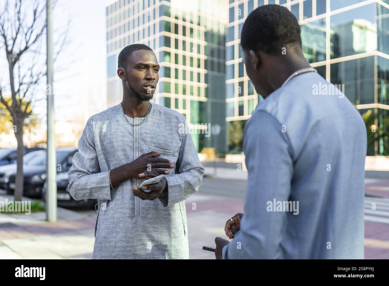 Deux hommes d'affaires sénégalais en tenue dashiki ont une conversation à l'extérieur, discutant potentiellement d'un accord commercial Banque D'Images