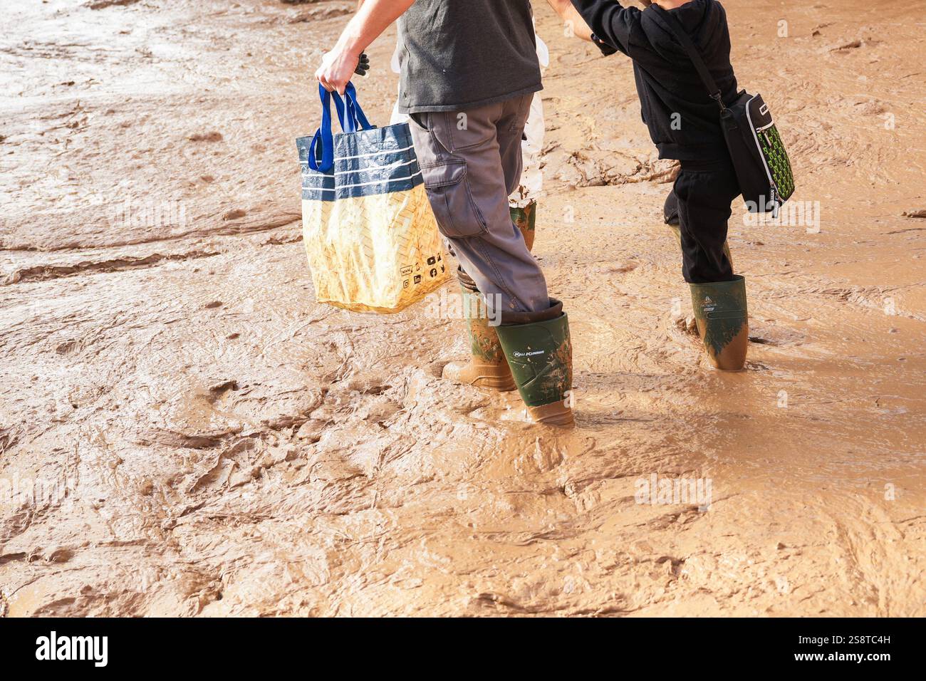 Père et fils marchent dans des bottes en caoutchouc coulant dans la boue dans une rue inondée avec des sacs dans leurs mains. Communauté valencienne, Espagne. Banque D'Images