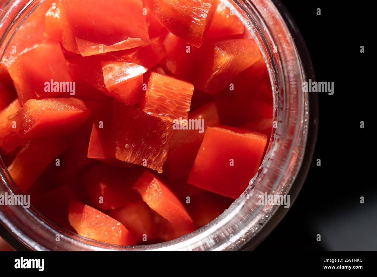 Une vue rapprochée de poivrons rouges fraîchement coupés en dés dans un bocal en verre, mettant en valeur leur couleur vibrante et leur texture croustillante sous la lumière naturelle. Banque D'Images