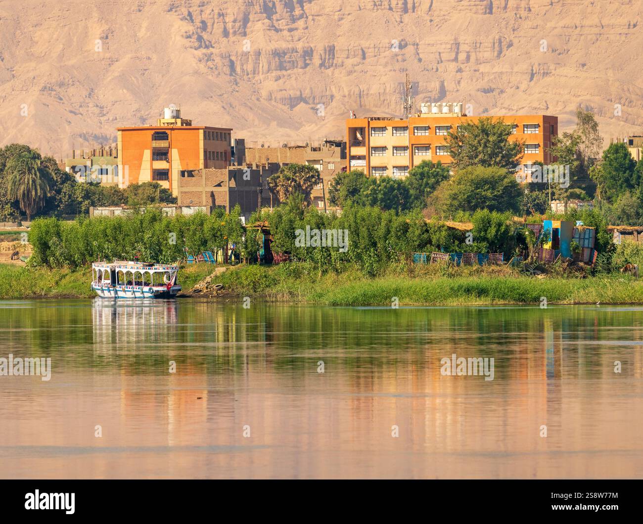 Une paisible ville riveraine de Naqadah en Égypte, avec des bâtiments traditionnels et une végétation luxuriante, avec le désert du Sahara derrière Banque D'Images