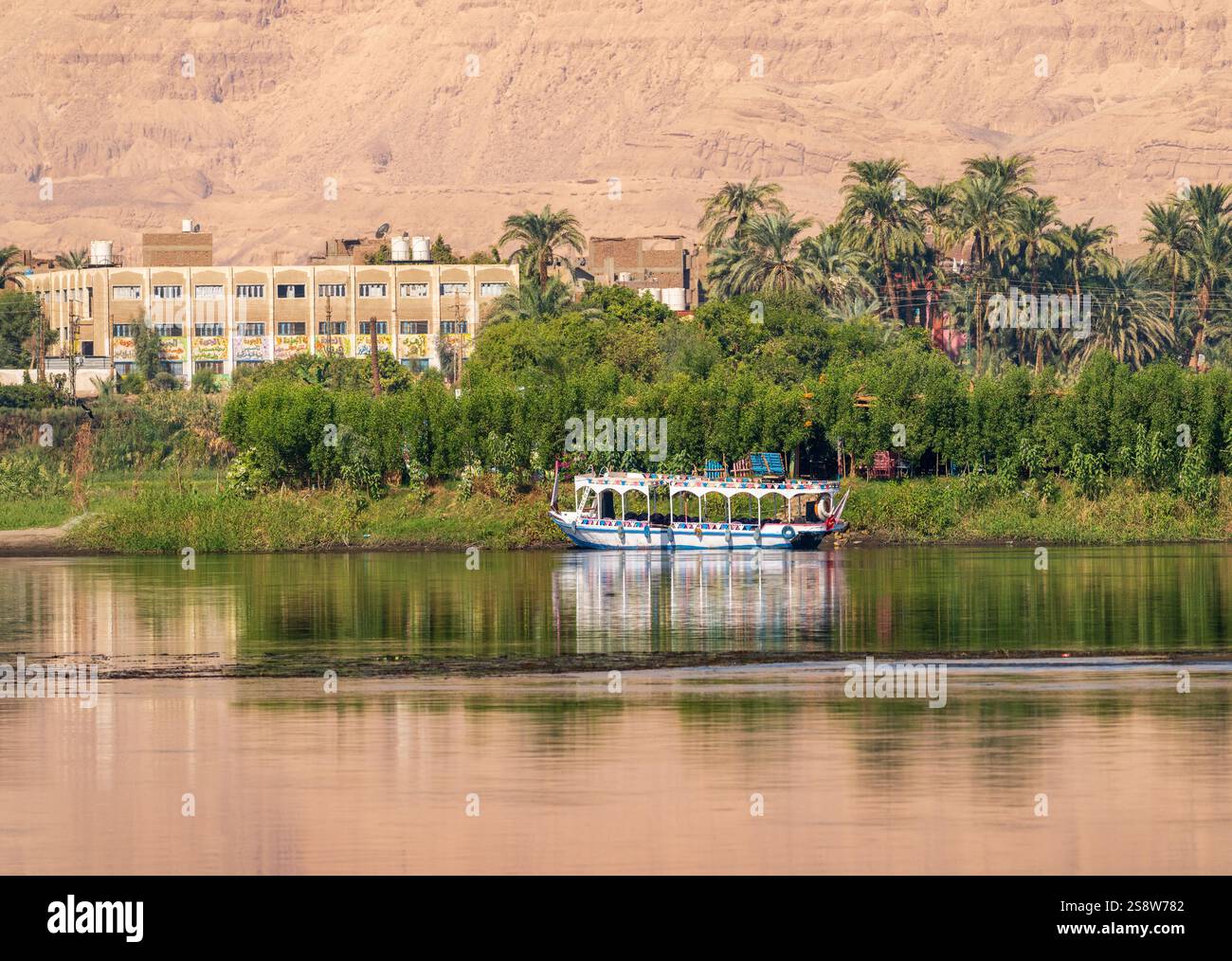 Une paisible ville riveraine de Naqadah en Égypte, avec des bâtiments traditionnels et une végétation luxuriante, avec le désert du Sahara derrière Banque D'Images