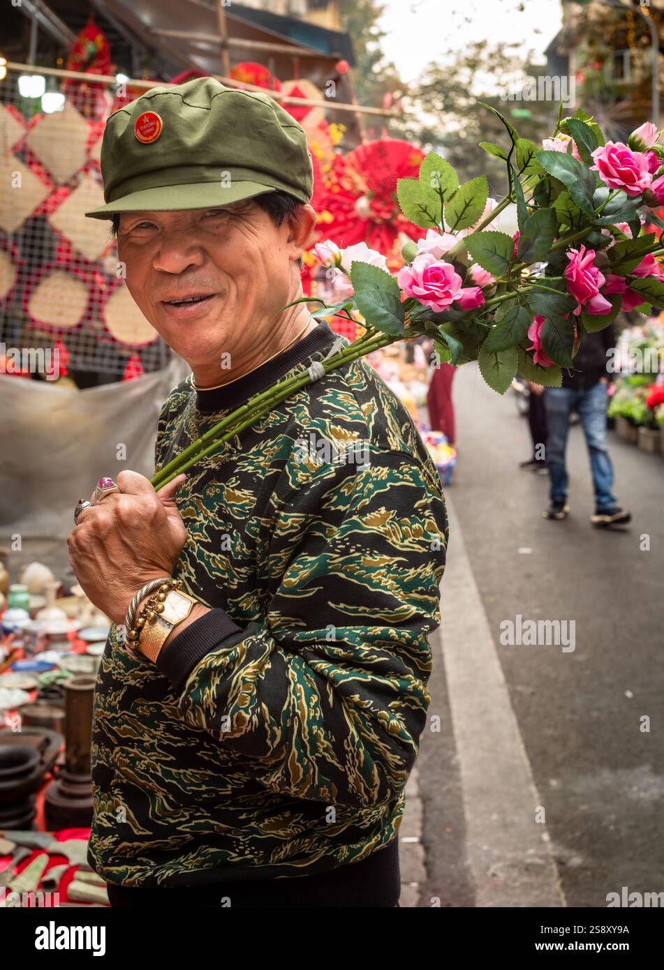 Un homme vietnamien vêtu de vêtements vert olive style armée tient un tas de roses artificielles sur son épaule à Hang Ruoi à Tet or luna Banque D'Images
