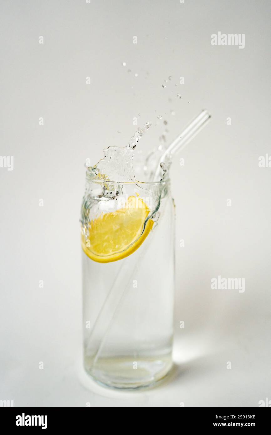 L'eau de citron éclaboussure dans le verre avec la paille écologique sur le bac blanc Banque D'Images