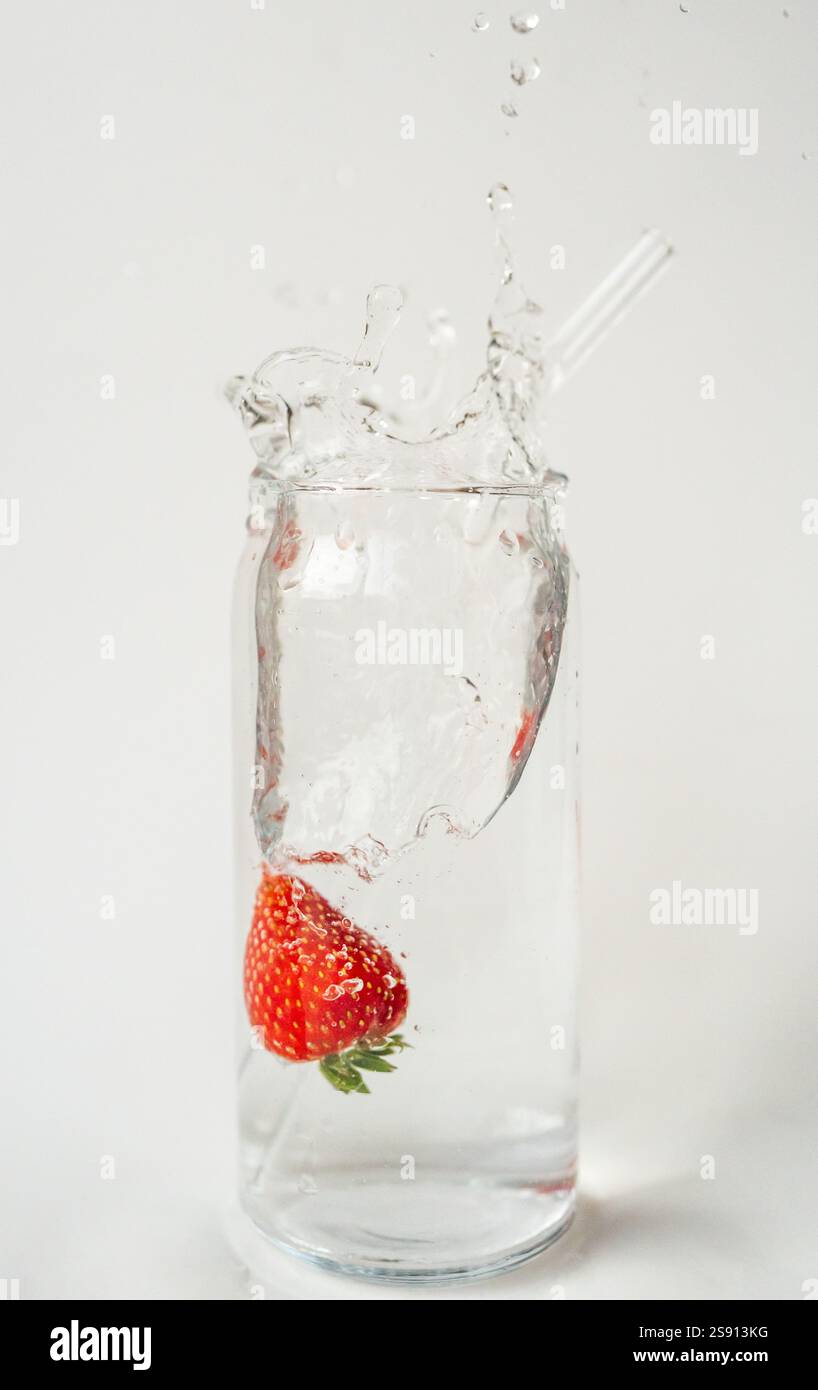 Éclaboussure de fraise dans un verre d'eau avec de la paille réutilisable sur blanc Banque D'Images