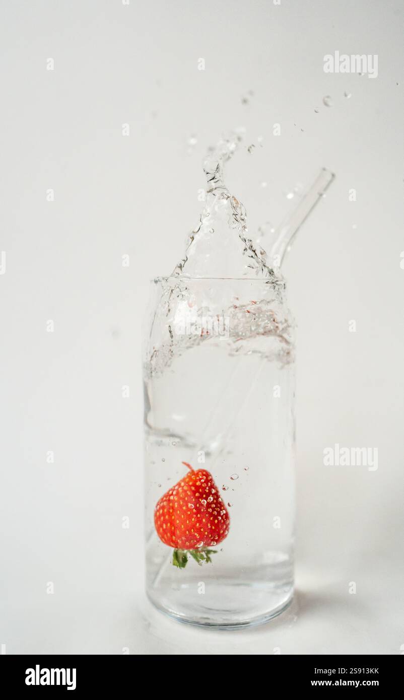 Éclaboussure de fraise dans un verre d'eau avec de la paille réutilisable sur blanc Banque D'Images