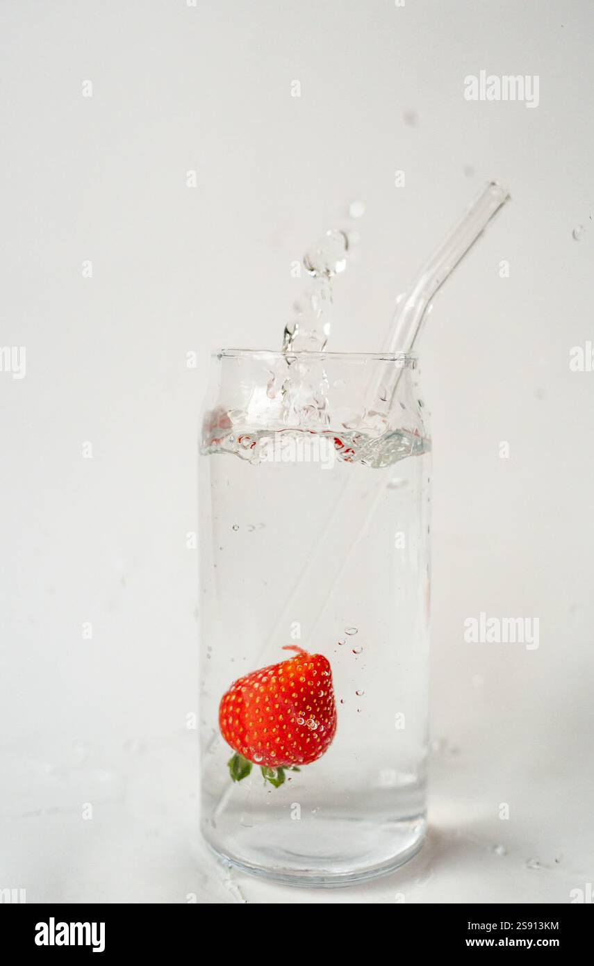 Éclaboussure de fraise dans un verre d'eau avec de la paille réutilisable sur fond blanc Banque D'Images