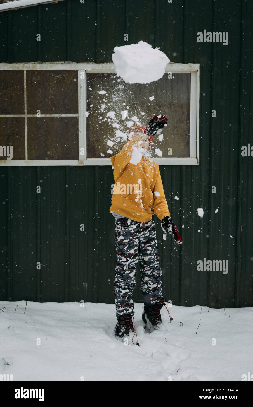 Enfant lançant une boule de neige géante le jour d'hiver Banque D'Images