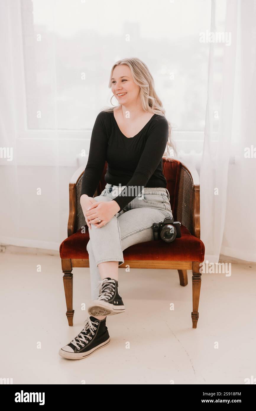 Femme souriante avec un appareil photo assis sur une chaise rouge Banque D'Images