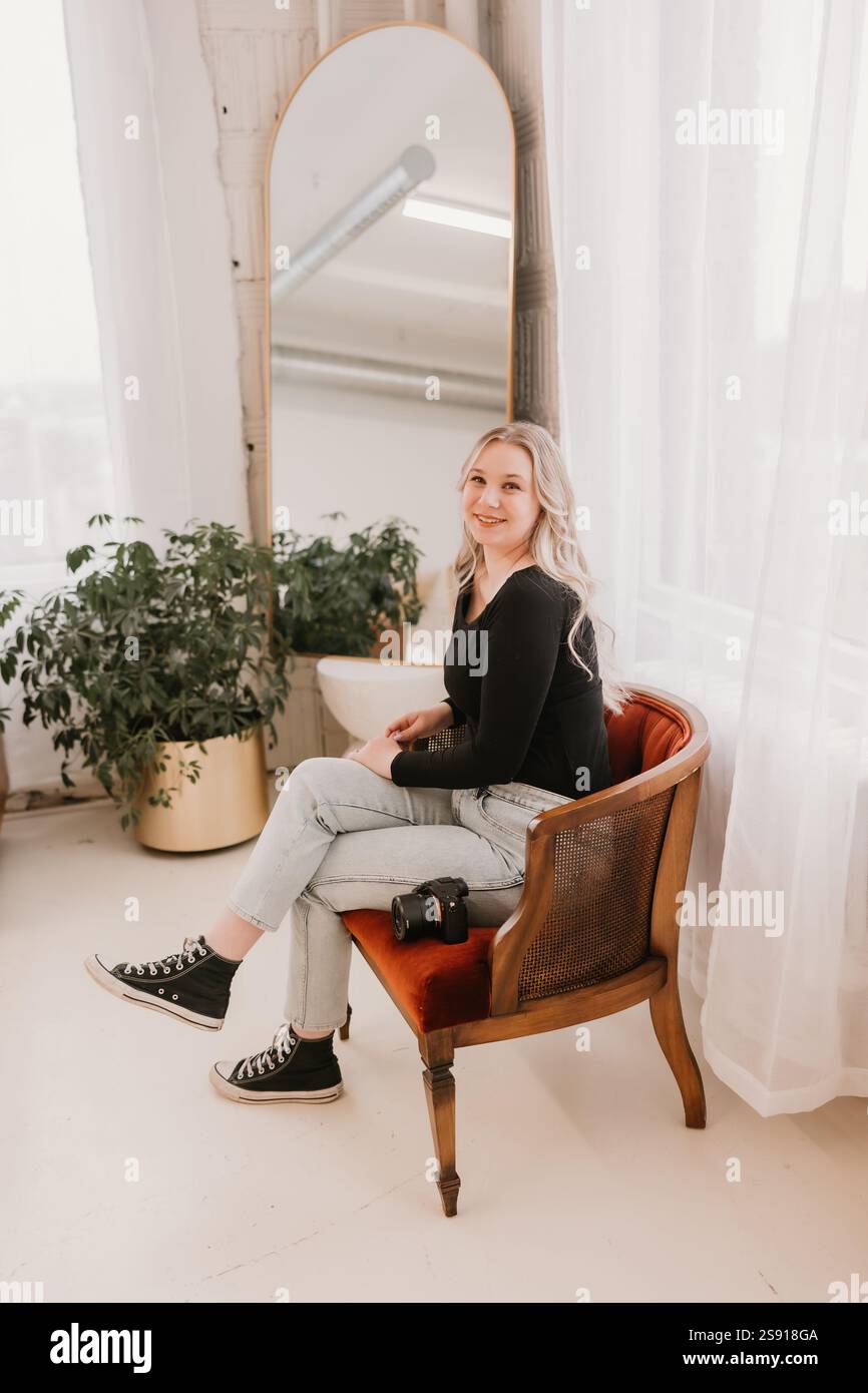 Femme souriante avec un appareil photo assis sur une chaise rouge. Banque D'Images